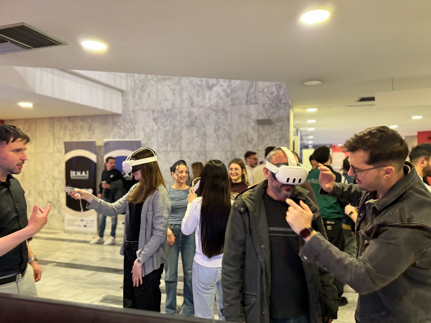 People using white VR headsets at a tech event in a marble floored lobby with onlookers nearby