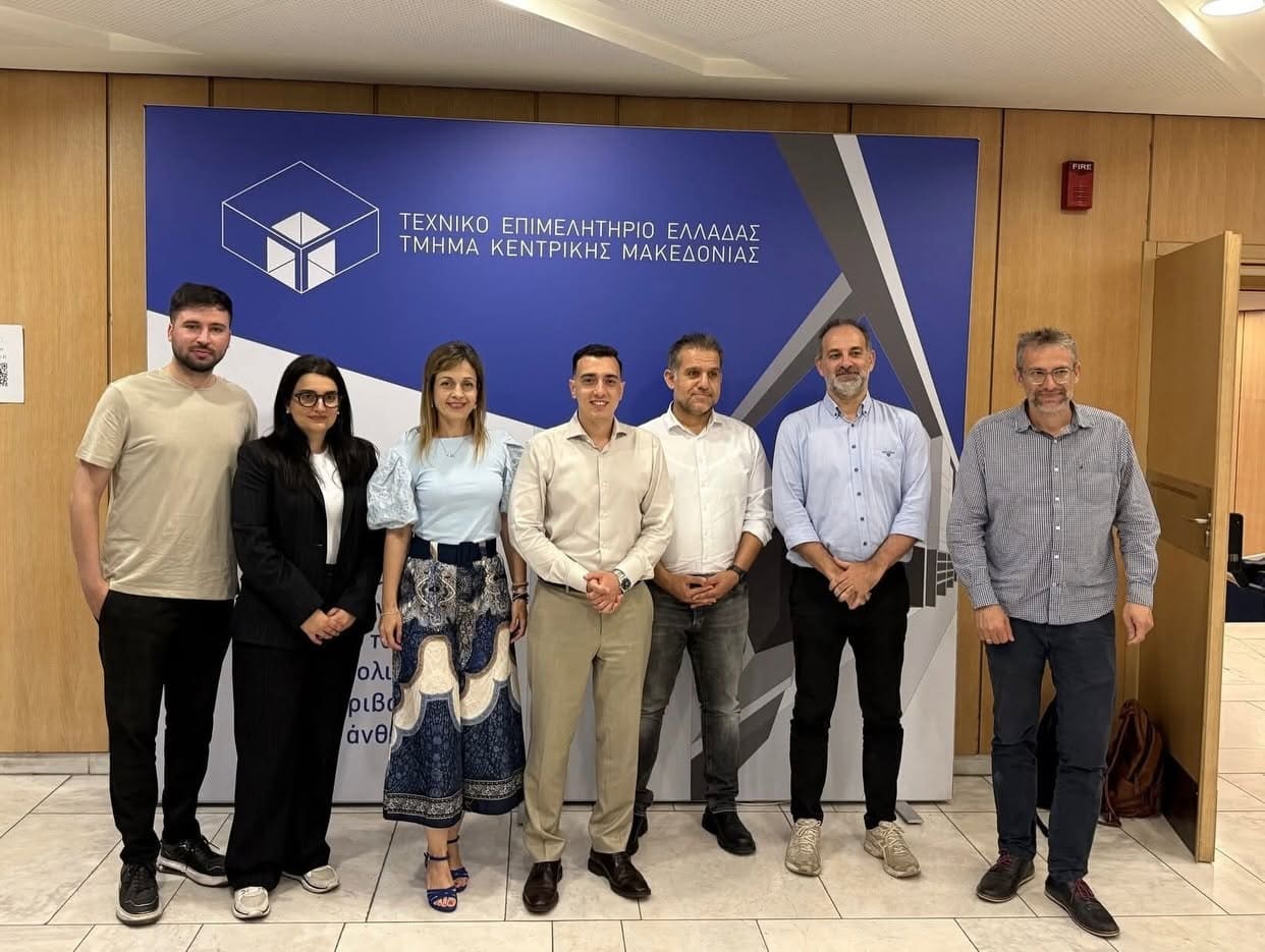 Seven professionals pose for a group photo in front of a blue banner with Greek text